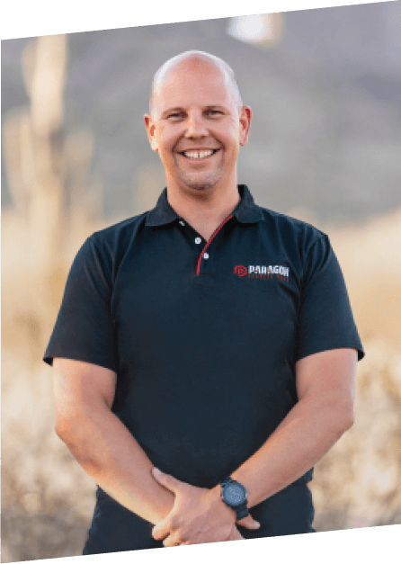 A bald man in a black polo shirt stands against a desert backdrop, showcasing the brand identity of Paragon Service Pros.