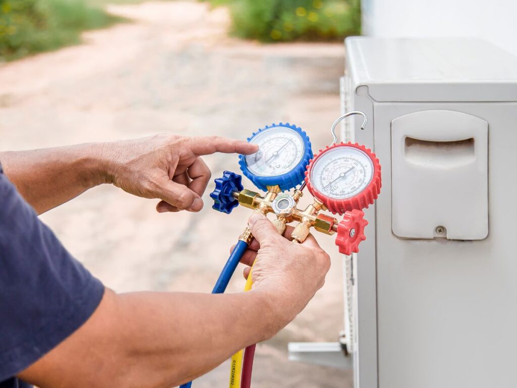 A technician holds a hose and gauge to perform a refrigerant check on an air conditioning unit