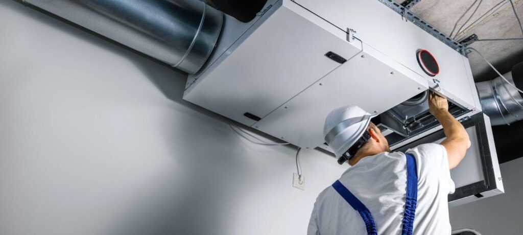 A man in a hard hat repairs a large air conditioning unit, showcasing his skills